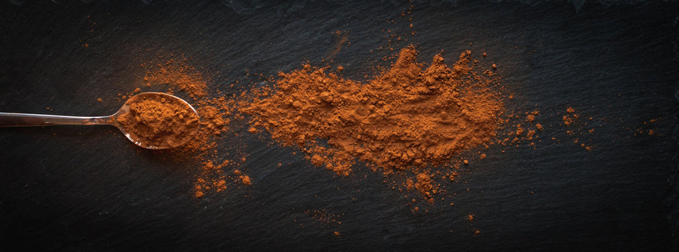 Ground cinnamon in teaspoon on dark background, top view, text space