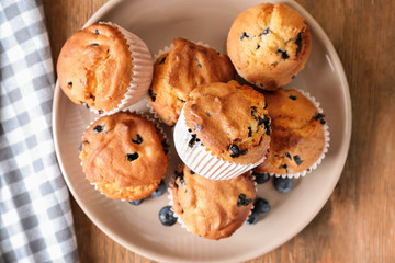 Plate with tasty blueberry muffins on wooden table