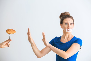 Woman with taped mouth refusing to eat unhealthy food on white background. Diet concept