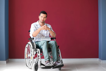 Male teacher in wheelchair with books near color wall