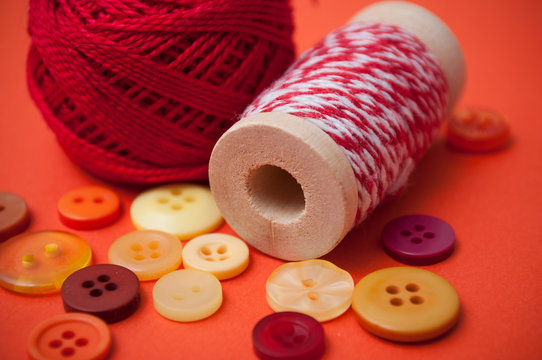 closeup of buttons and bobbins of cotton yarn on orange background