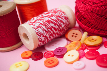 closeup of buttons and bobbins of cotton yarn on pink background
