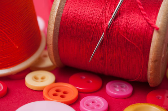 closeup of buttons and bobbins of cotton yarn on red background