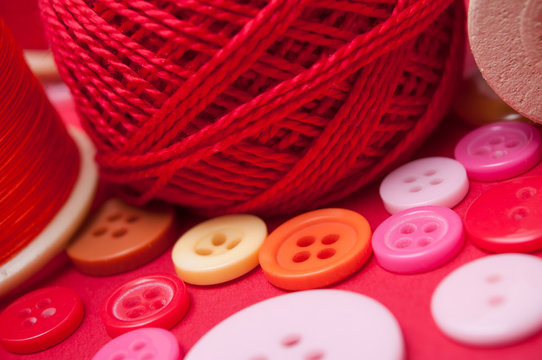closeup of buttons and bobbins of cotton yarn on red background