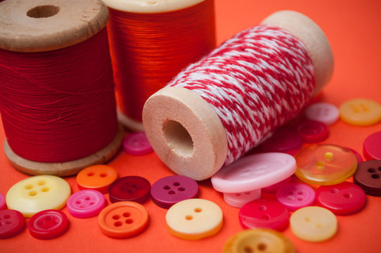 closeup of buttons and bobbins of cotton yarn on orange background