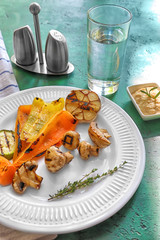 Plate with tasty grilled vegetables on color table