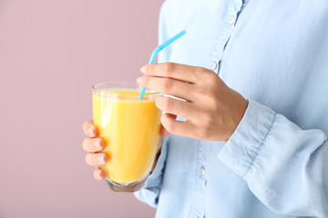 Woman holding glass of tasty yellow smoothie on color background, closeup