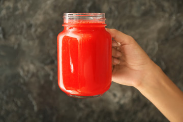 Woman holding mason jar of tasty red smoothie on grey background