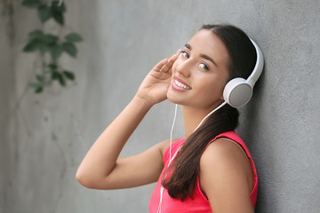 Naklejka premium Smiling young woman enjoying music with white headphones, leaning against a gray wall outdoors