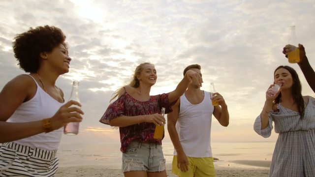 party, summer holidays and people concept - group of happy friends with non alcoholic drinks dancing on beach