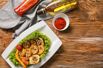 Plate with tasty grilled vegetables and tomato sauce on wooden table