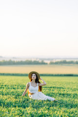 Girl walking on the field, in a hat and summer dress. Smiling and laughing, beautiful sunset in the forest and in nature. Happy traveler, lifestyle.