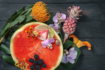 Composition with fresh tropical flowers and half of ripe watermelon on wooden background - Powered by Adobe