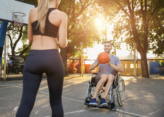 Young man in wheelchair and sporty woman training with ball outdoors