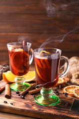 Glass cups of delicious hot mulled wine on wooden board