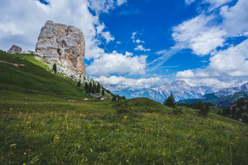 Famous Dolomiti landmark, Cinque Torri. Rock towers in green meadows and pastures of Dolomiti, blue sky with dramatic clouds. Trekking, hiking and climbing area. Alpine landscape.