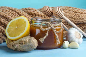 Garlic, a honey jar, ginger, lemon and honey spoons on a blue background. Maintenance of immunity. Treatment of colds and flu. Products for immunity. Immunity concept.