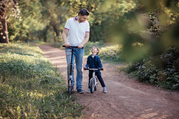 Obraz premium father riding kickscooter and son on the bicycle