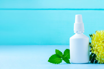 Spray from the common cold, stuffy nose, leaf of fresh mint and flower on a blue background. Treatment of colds and flu. Throw off an illness. Medication with menthol. Copy space