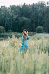 Beautiful Russian girl in a hat and summer dress, walking on the field in the grass to the waist. Happy traveler