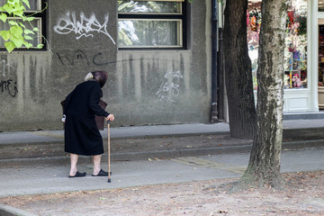 A very old woman walks down the street with a wand