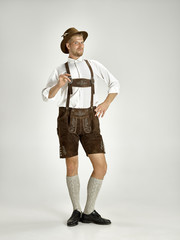 Portrait of Oktoberfest young man in hat, wearing a traditional Bavarian clothes standing at full-length at studio. The celebration, oktoberfest, festival concept