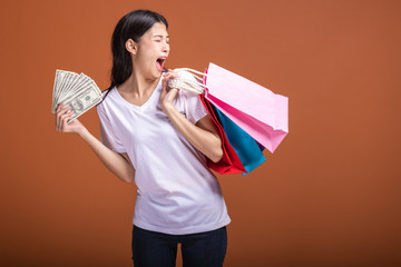 Woman holding shopping bag and cash isolated in orange background.