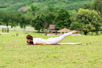 Beautiful Attractive Asian woman practice yoga Locust or Shalabhasana pose with yoga meditation relax and refresh health on Meadow feeling happiness and comfortable in garden