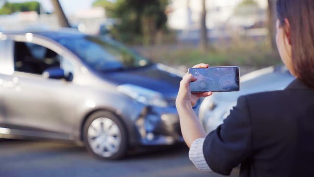 A female insurance agent taking photo of car accident on her smartphone. Two broken cars after car accident standing on the road. 4K UHD.