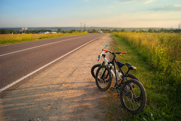 Obraz premium Bicycle tourism. Mountain bikes on a evening sunny light at the edge of the road, fields and landscape. Active freedom rest on vacation
