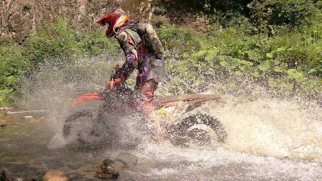 Enduro Motocycle Rider Crosses Mountain River Splashes of Water and Dirt. Slow Motion.
