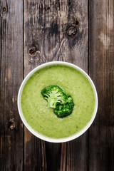 Homemade broccoli cream soup in white bowl with toasts on wooden background