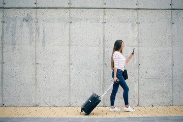 Woman carrying luggage and using smart phone while walking to the station.