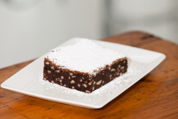 a brownie on a square plate with powdered sugar on top