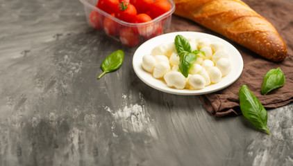 Mozzarella with basil leaves - fresh ingredients for Bruschetta, with cherry tomatoes and French baguette with copy space on a dark background, top view