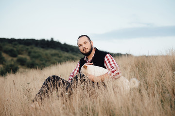 a male hipster sits in a park with a dog