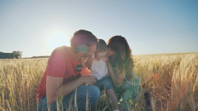 Happy family having fun and laughing on a spring summer day at sunset. Parents funny kiss their son.