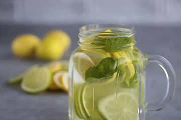 Refreshing lemonade with lemon and lime slices and mint leaves in a glass mug on a gray background.