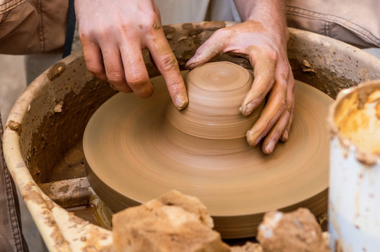 Hands of a young man creating a clay jar on a potter's wheel