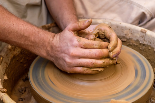 Hands of a young man creating a clay jar on a potter's wheel