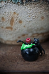 Halloween black cat. A Halloween black cat making magic potion with poison red apple on top. Abstract background of old damaged wall with dim light. Grunge & grained filter. Soft focus on cat's eye. 