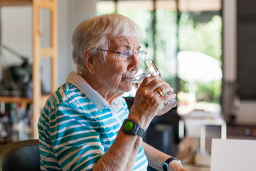 Elderly woman drinking water at home