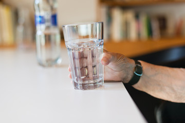 Hand of senior lady holding a glass of water on table