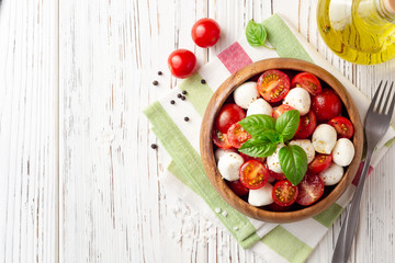 Italian caprese salad with cherry tomatoes, mozzarella cheese and basil on white wooden background