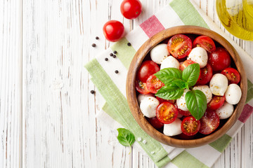 Italian caprese salad with cherry tomatoes, mozzarella cheese and basil on white wooden background
