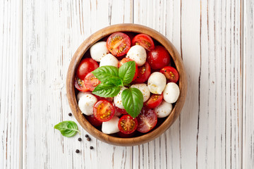 Italian caprese salad with cherry tomatoes, mozzarella cheese and basil on white wooden background