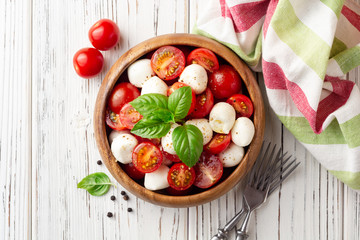 Italian caprese salad with cherry tomatoes, mozzarella cheese and basil on white wooden background