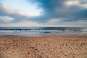 Blurry long exposure of unidentifiable surfers on a beach with fading light and copy space