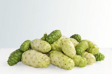 Noni fruit or Morinda Citrifolia noni pile on white table with isolated gray background. With copy space for text and with clipping path.