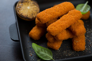 Closeup of fried fish sticks or breaded fish fillet snack in a cast-iron serving pan, selective focus